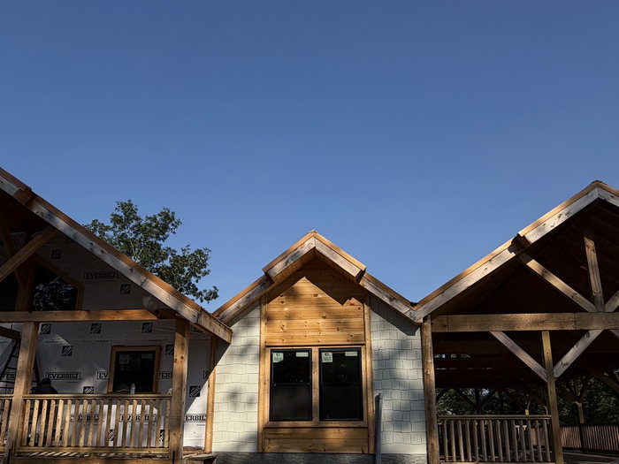 Three cabin gables in a row, timber-frame trusses set and cedar siding going on.